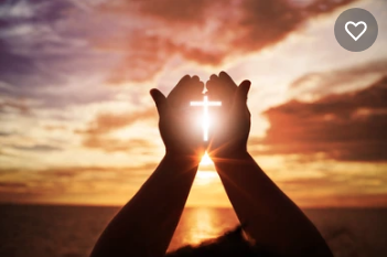 Cross of light shining through cupped hands in front of a setting sun